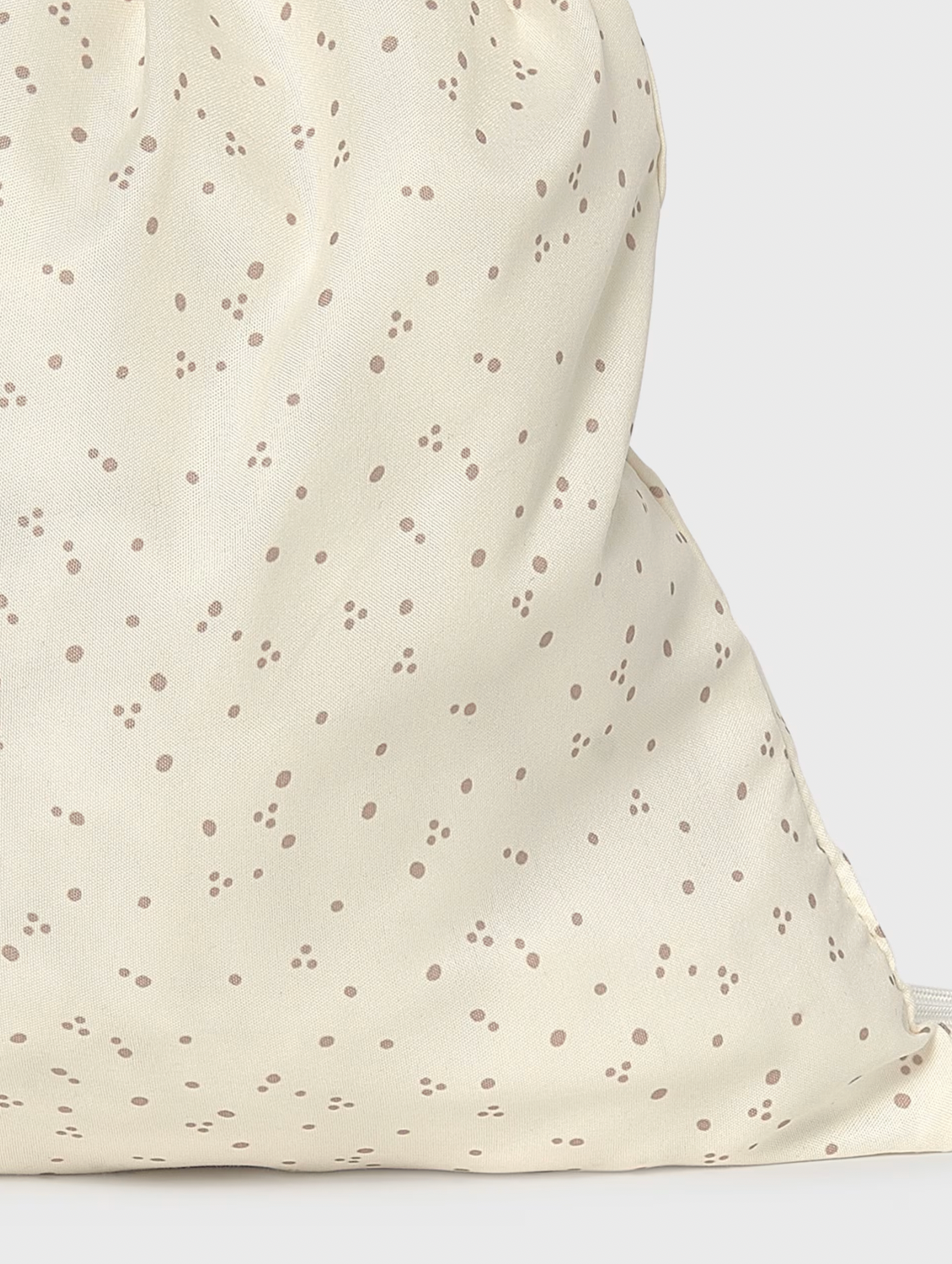 Close-up of a cream-colored fabric drawstring bag with a scattered brown polka dot pattern, showing the soft texture and drawstring closure.