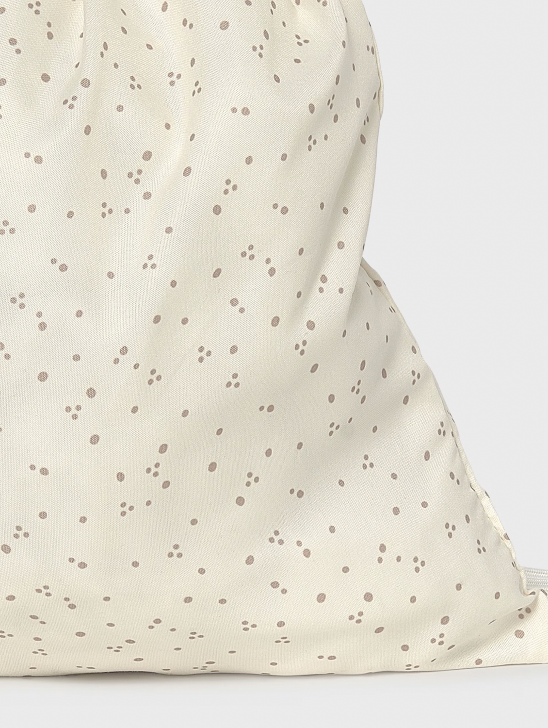 Close-up of a cream-colored fabric drawstring bag with a scattered brown polka dot pattern, showing the soft texture and drawstring closure.