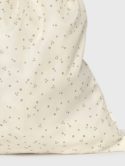 Close-up of a cream-colored fabric drawstring bag with a scattered brown polka dot pattern, showing the soft texture and drawstring closure.