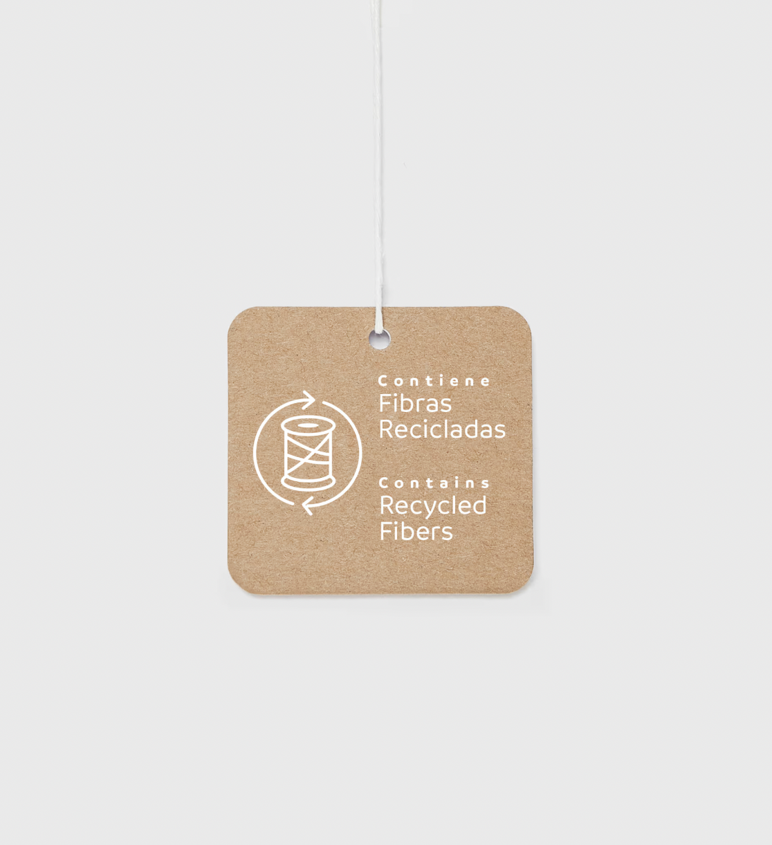 A square kraft paper hang tag with rounded corners, featuring white text that reads 'Contiene Fibras Recicladas / Contains Recycled Fibers' alongside a spool icon, suspended by a thin white string against a light gray background.