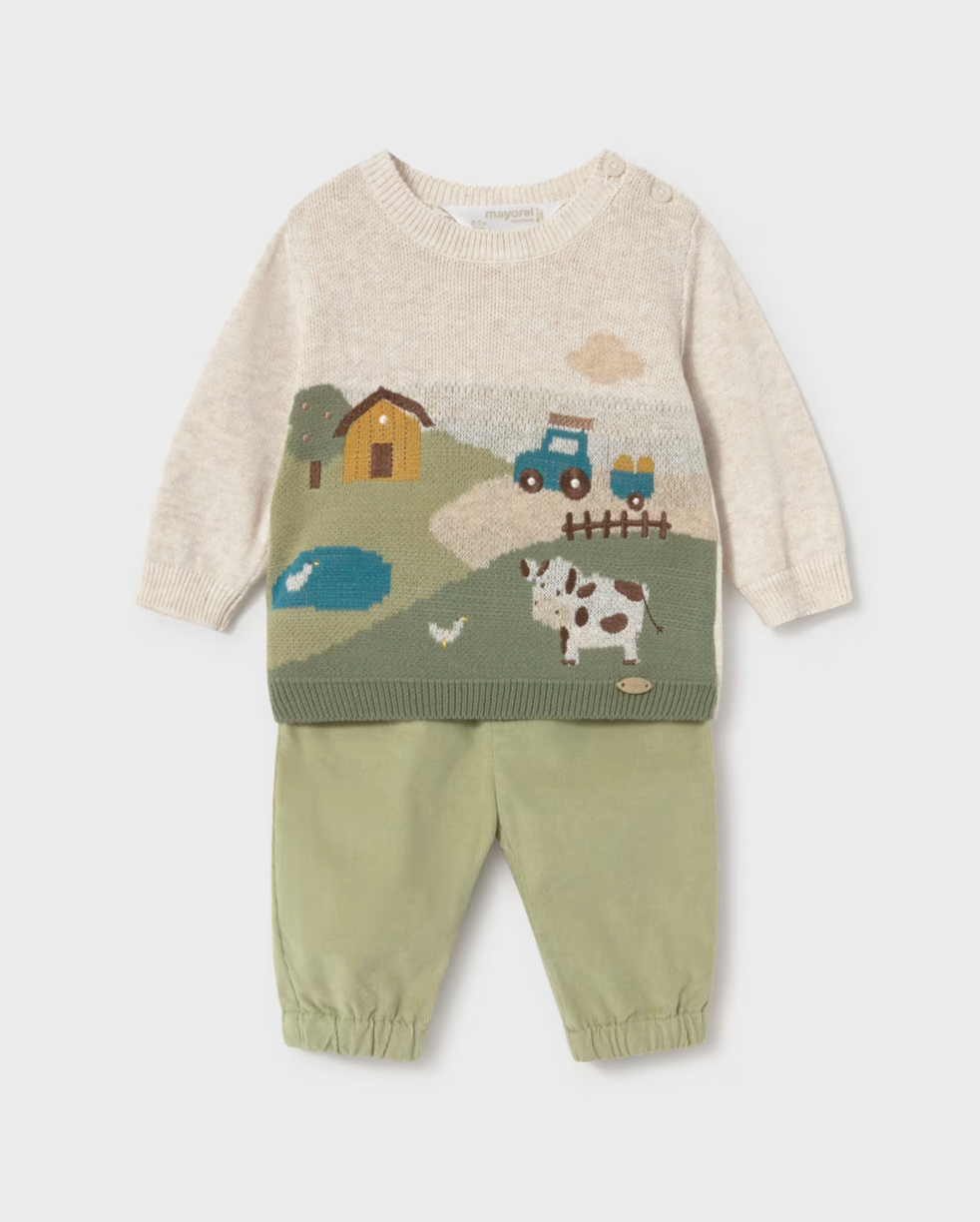 A baby knit two-piece outfit featuring a cream-colored long-sleeve sweater with a colorful farm landscape graphic (including a tractor, barn, pond, and cow) paired with sage green pants with elastic cuffs.