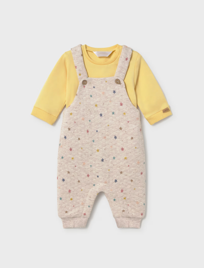A baby's long-sleeve romper featuring cream-colored microfiber overall with a colorful star pattern, worn over a soft yellow long-sleeve shirt. The romper has adjustable shoulder straps with two brown buttons and ribbed cuffs and ankles.
