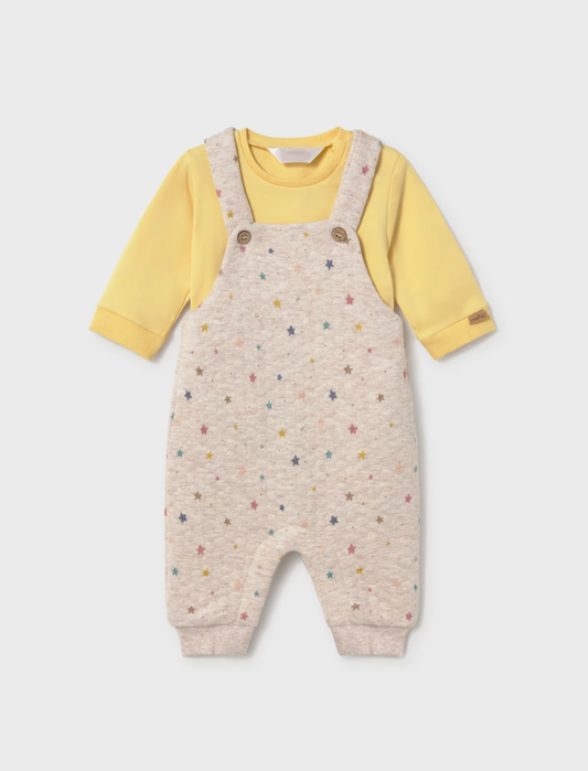 A baby's long-sleeve romper featuring cream-colored microfiber overall with a colorful star pattern, worn over a soft yellow long-sleeve shirt. The romper has adjustable shoulder straps with two brown buttons and ribbed cuffs and ankles.