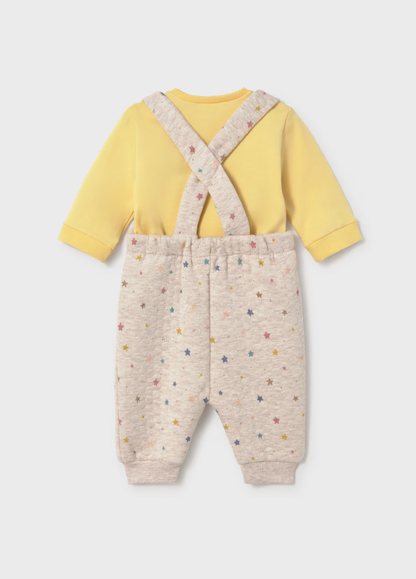 A baby two-piece outfit featuring a pale yellow long-sleeve top and light beige heathered pants with a multicolor star print and crossover suspenders, shown from the back on a light gray background.