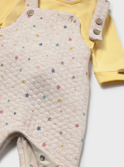 A baby's long-sleeve romper set featuring a cream-colored honeycomb quilted bib overlayer with a scattered pastel star pattern, worn over a soft yellow long-sleeve bodysuit. The bib has buttoned shoulder straps and snap closures at the crotch.
