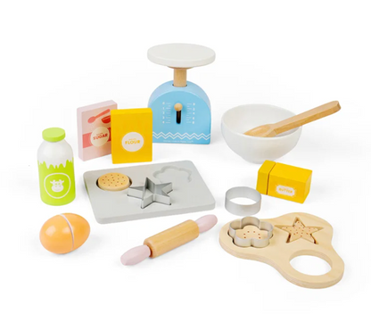 A children's wooden play kitchen baking set arranged on a white background. The set includes a blue scale, white bowl with wooden spoon, milk bottle, flour box, sugar box, cookie cutters, rolling pin, egg, and other small baking accessories.