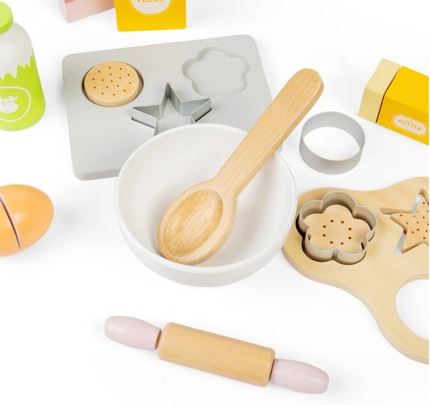 A children's wooden toy kitchen set arranged on a white background, including a white bowl, wooden spoon, rolling pin, cookie cutters, mold, and play food pieces.