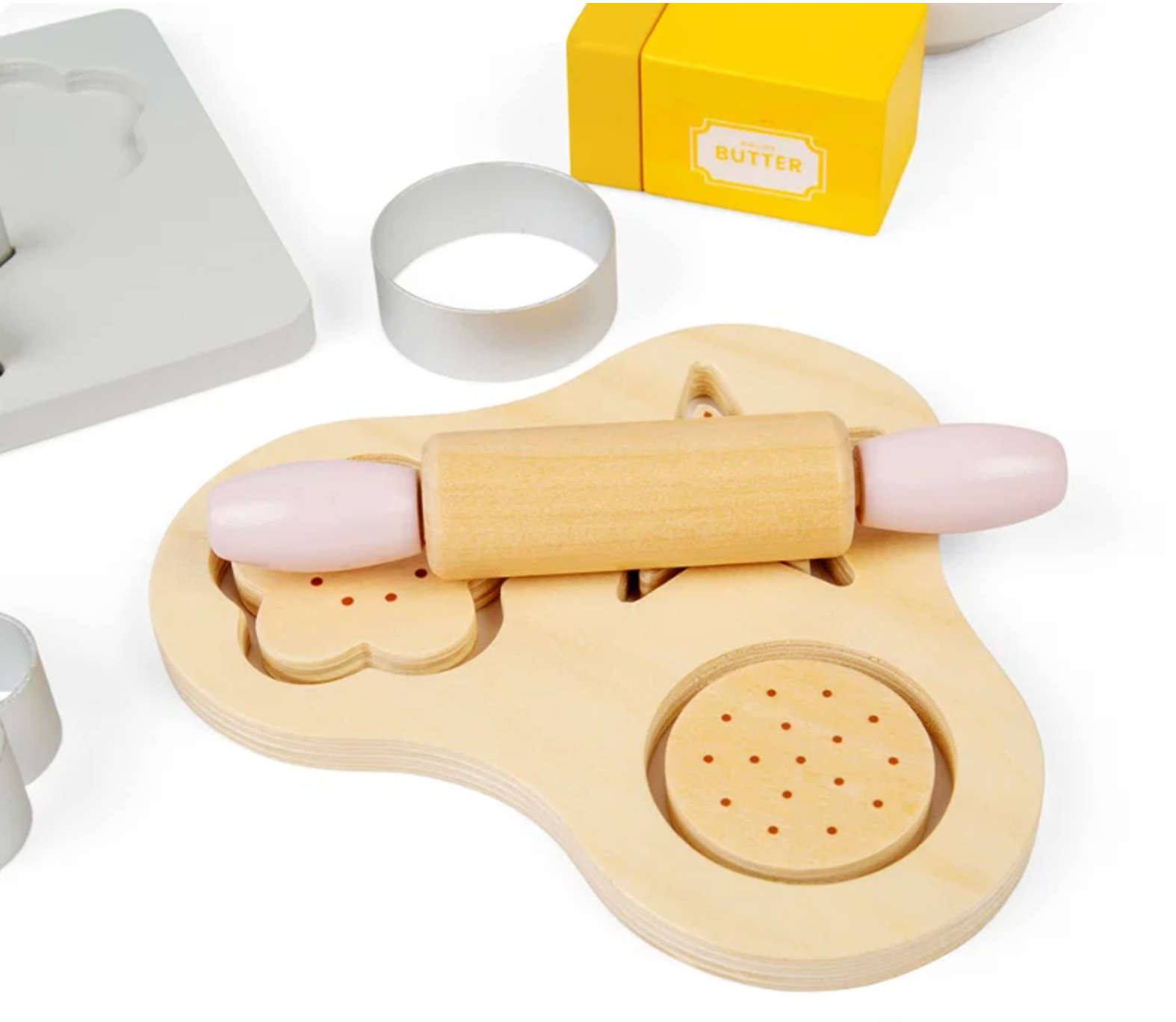 A wooden toy cookie cutter and rolling pin set on a white background, with a yellow box labeled BUTTER and metal cutter rings nearby.