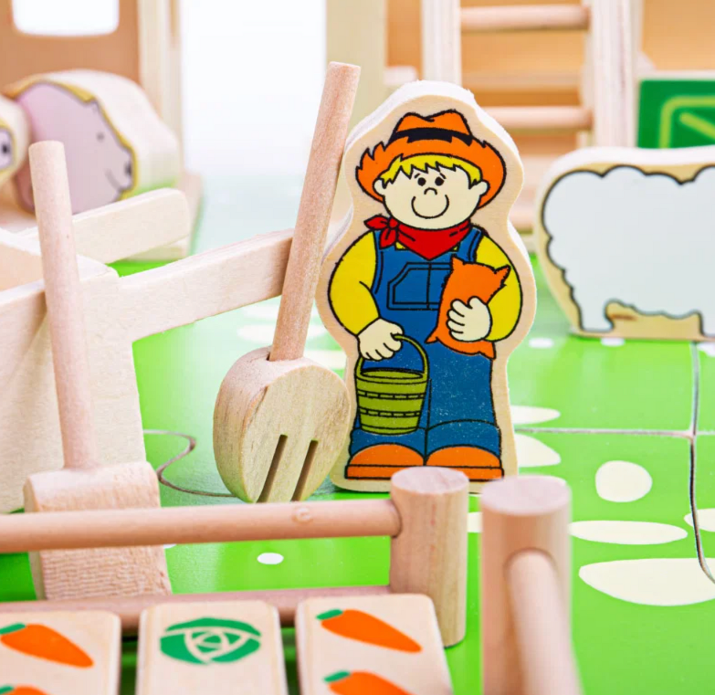 A close-up of a wooden farm playset with colorful wooden animal and character pieces, including a farmer holding a cat and a green board with natural wood components.