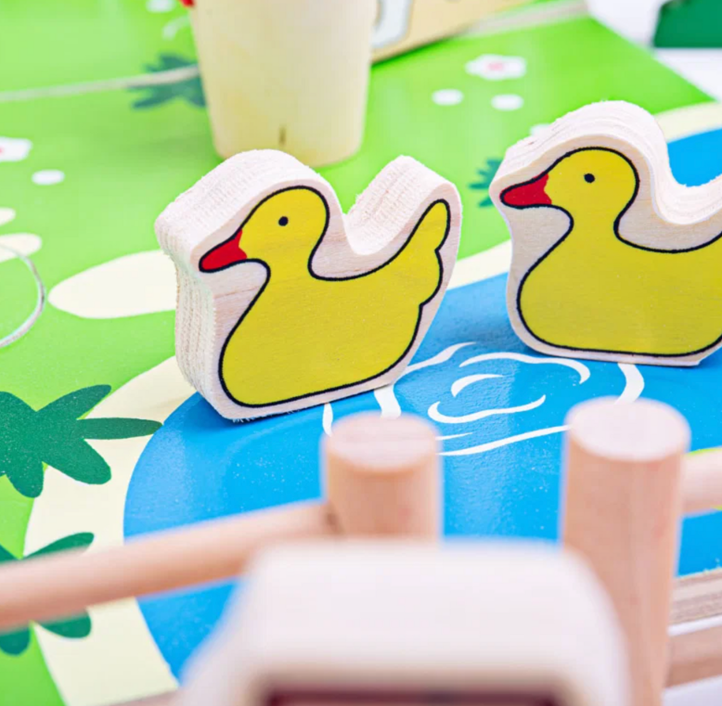 Two yellow duck-shaped wooden blocks with red beaks and black outlines, resting on a colorful green and blue children's play mat.
