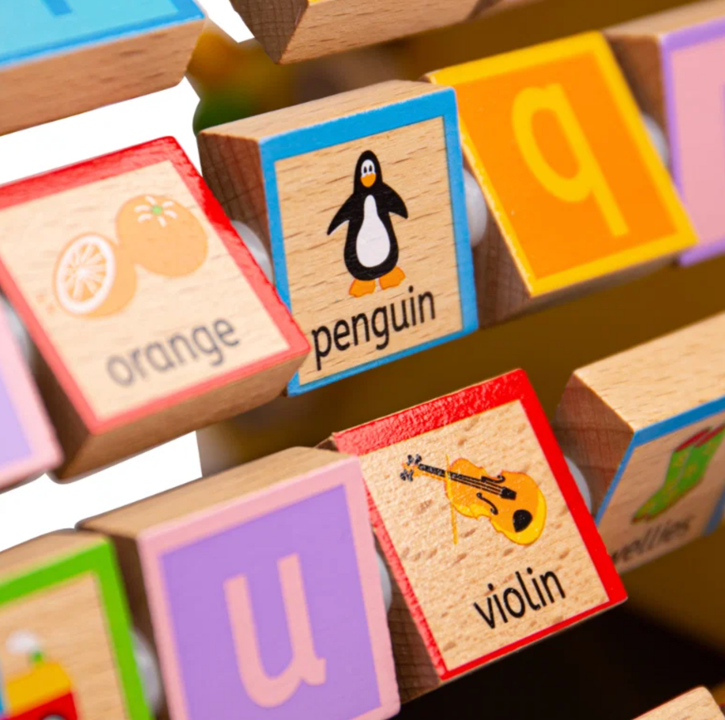 Close-up of wooden alphabet blocks with colorful borders and printed illustrations, including orange, penguin, letter q, violin, and letter u.