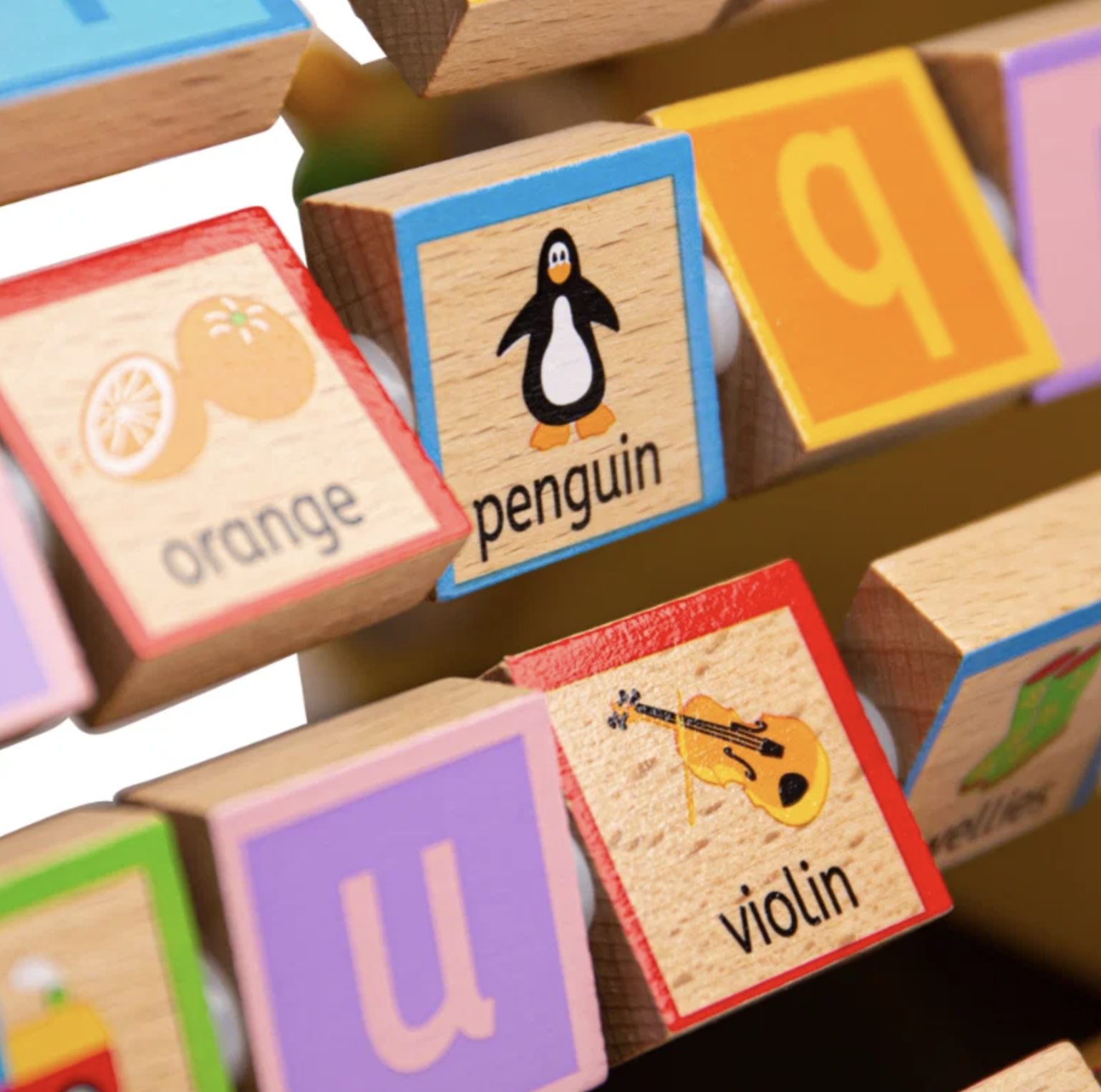 Close-up of wooden alphabet blocks with colorful borders and printed illustrations, including orange, penguin, letter q, violin, and letter u.