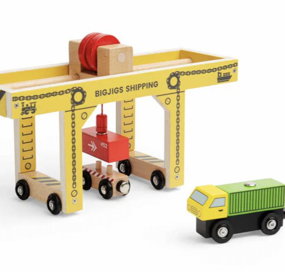 A wooden toy shipping crane set with a yellow and natural wood crane, a red crane hook, and a small yellow and green cargo truck on a white background.