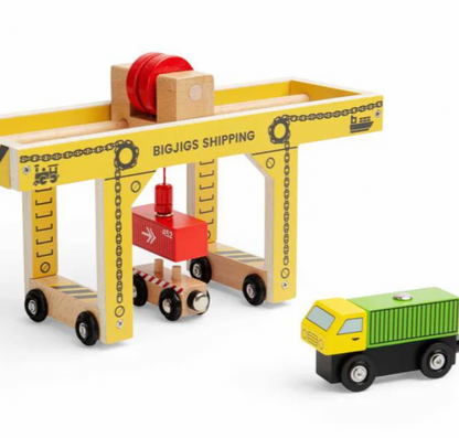A wooden toy shipping crane set with a yellow and natural wood crane, a red crane hook, and a small yellow and green cargo truck on a white background.