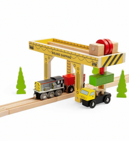 A wooden toy shipping crane set with a yellow and natural wood crane, a red crane hook, and a small yellow and green cargo truck on a white background.