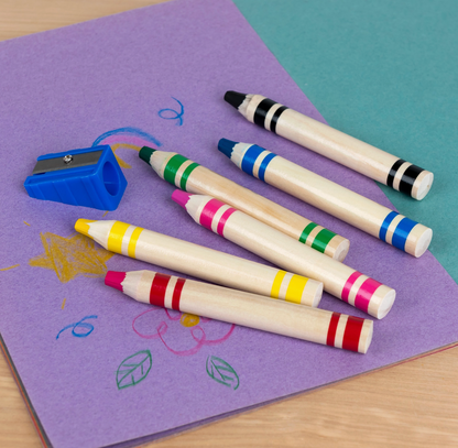 Six Rex London jumbo wooden crayons and blue sharpener laid out on purple paper with children's drawings
