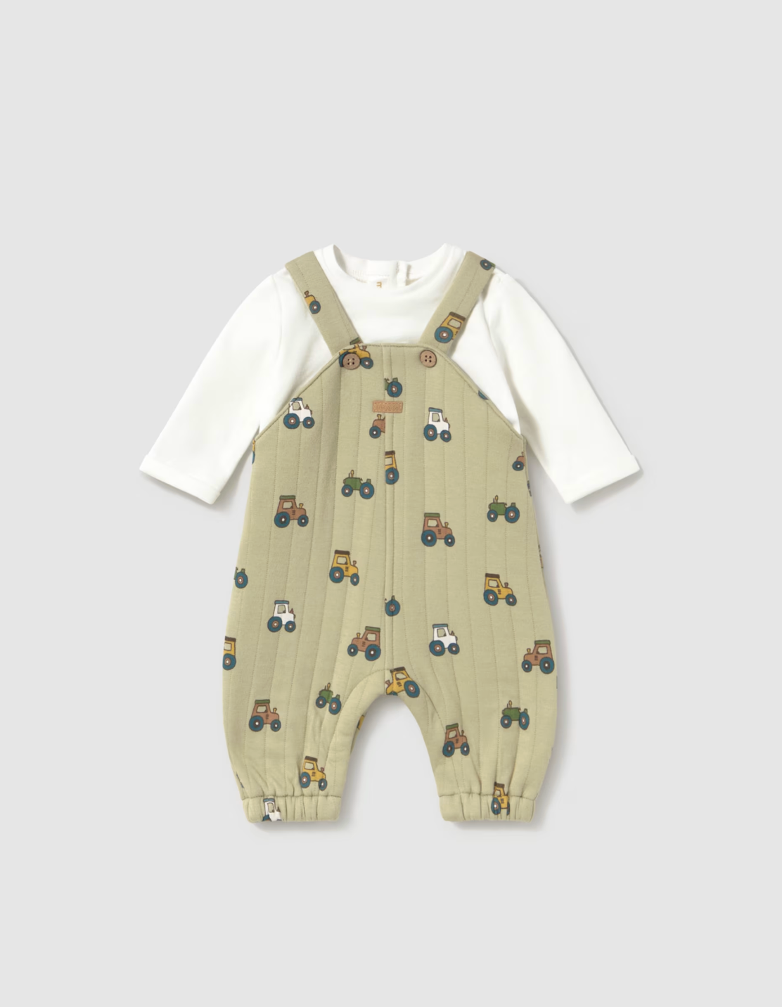 A baby's long-sleeve overall romper featuring a light beige/khaki body with a repeating tractor print, layered over a white long-sleeve shirt, displayed on a neutral gray background.