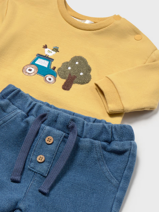A baby clothing set featuring a long-sleeve top in mustard yellow with an applique design of a blue truck and a tree, paired with blue corduroy pants with a buttoned pocket and drawstring.