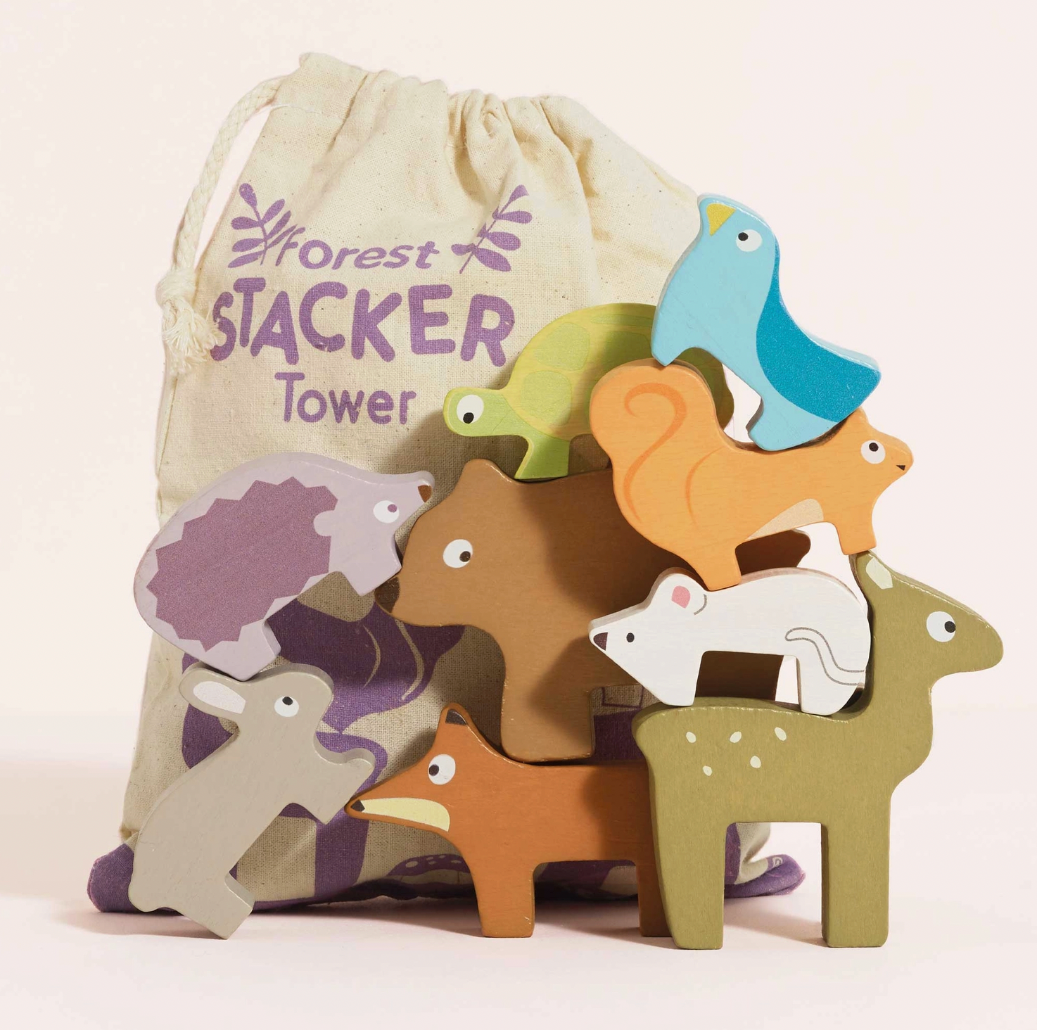 Le Toy Van Forest Stacking Wooden Animals set — lifestyle shot showing all 9 wooden animals tumbling out of the cotton drawstring bag printed with "Forest Stacker Tower" in purple, including bear, fox, squirrel, fawn, blue bird, rabbit, hedgehog, white mouse, green tortoise and raccoon