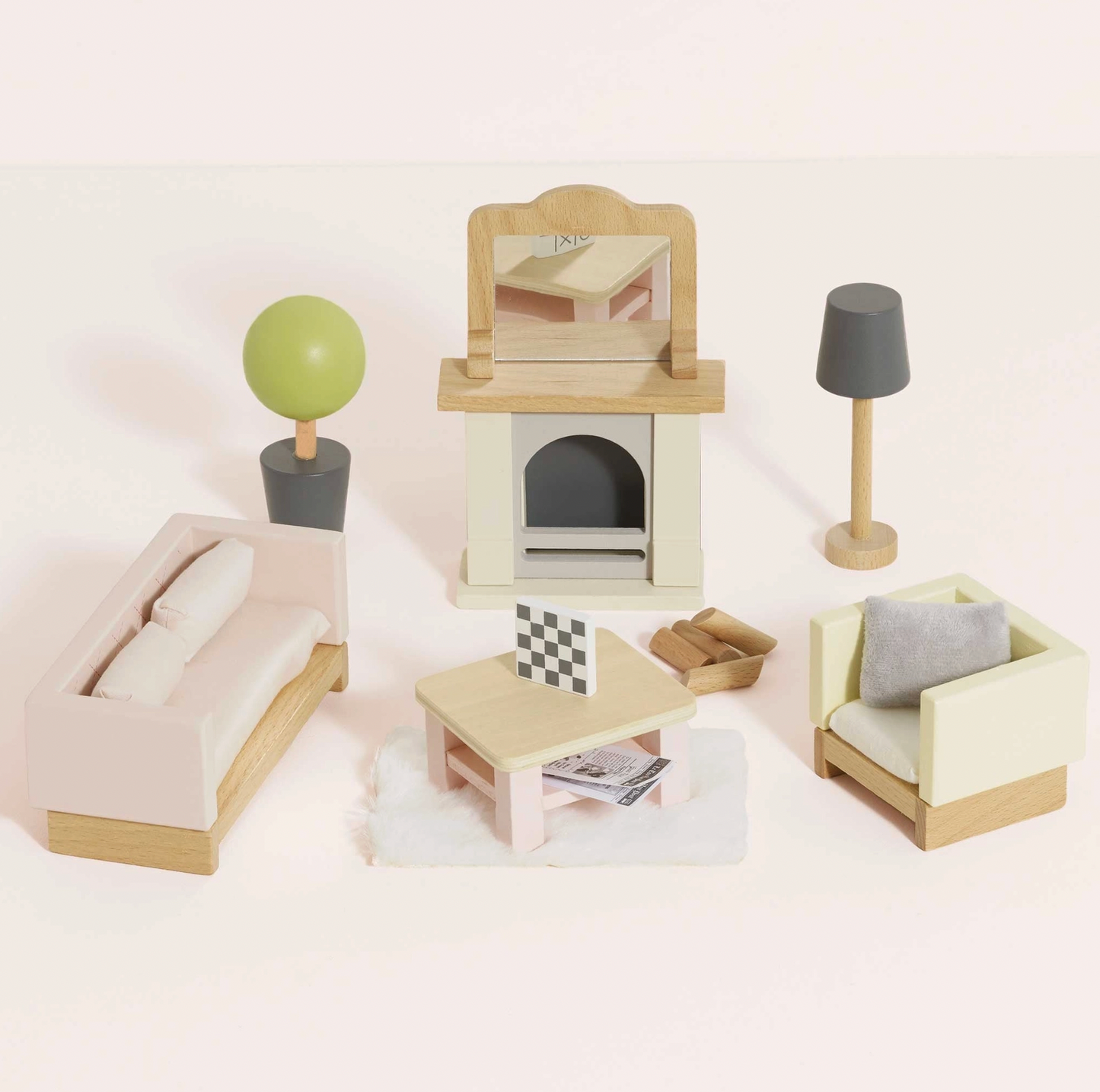 Le Toy Van 18-piece sitting room dolls house furniture set — styled scene showing blush pink quilted sofa, cream armchair with grey cushion, fireplace with mantel mirror and wooden logs, coffee table with chessboard, slate grey floor lamp and round topiary tree in dark grey pot