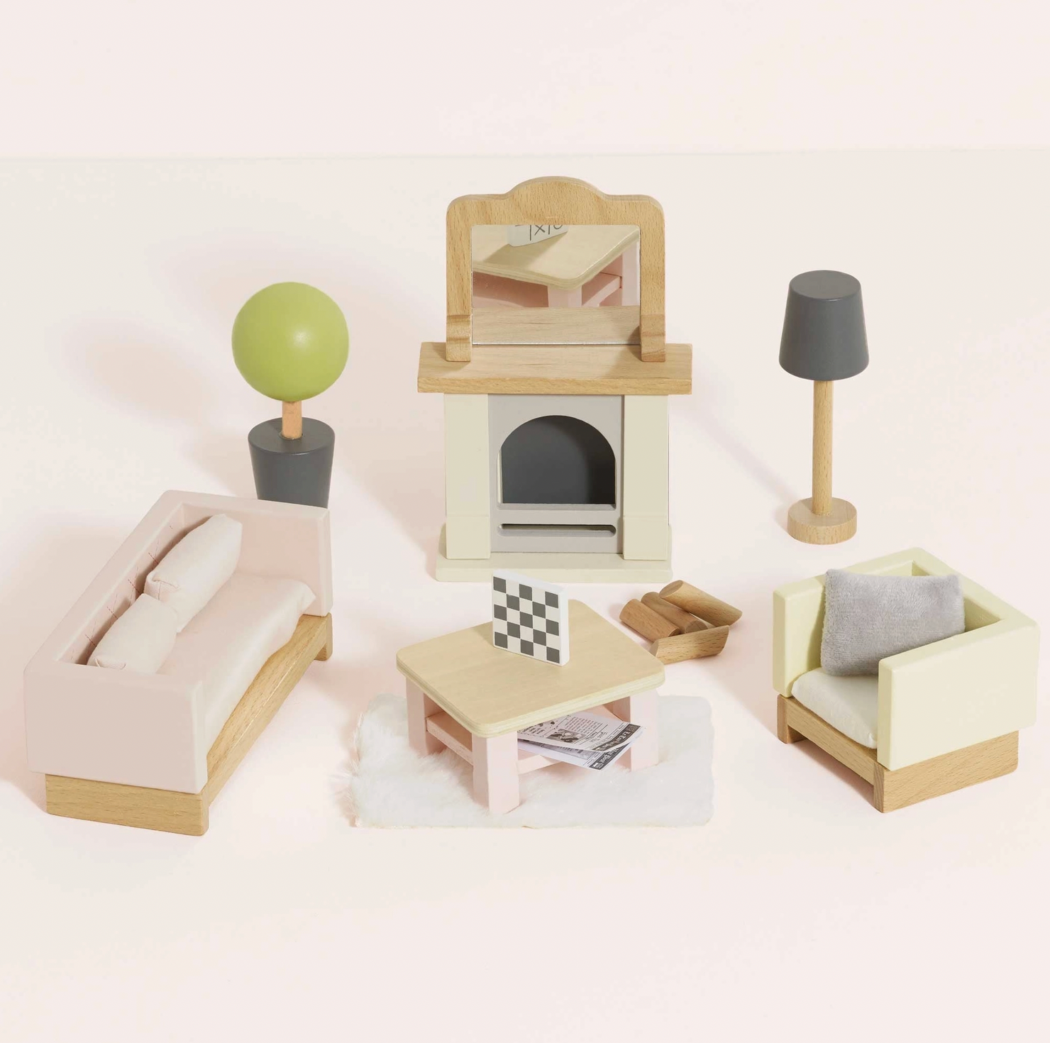 Le Toy Van 18-piece sitting room dolls house furniture set — styled scene showing blush pink quilted sofa, cream armchair with grey cushion, fireplace with mantel mirror and wooden logs, coffee table with chessboard, slate grey floor lamp and round topiary tree in dark grey pot