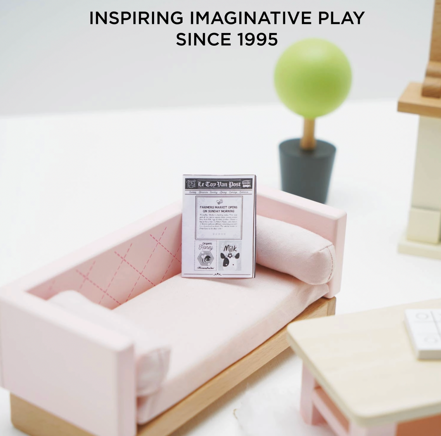 Le Toy Van sitting room dolls house furniture set — close-up lifestyle detail showing the blush pink quilted sofa with bolster cushion and miniature Le Toy Van Post newspaper, with round topiary tree in dark grey pot, "Inspiring Imaginative Play Since 1995" text