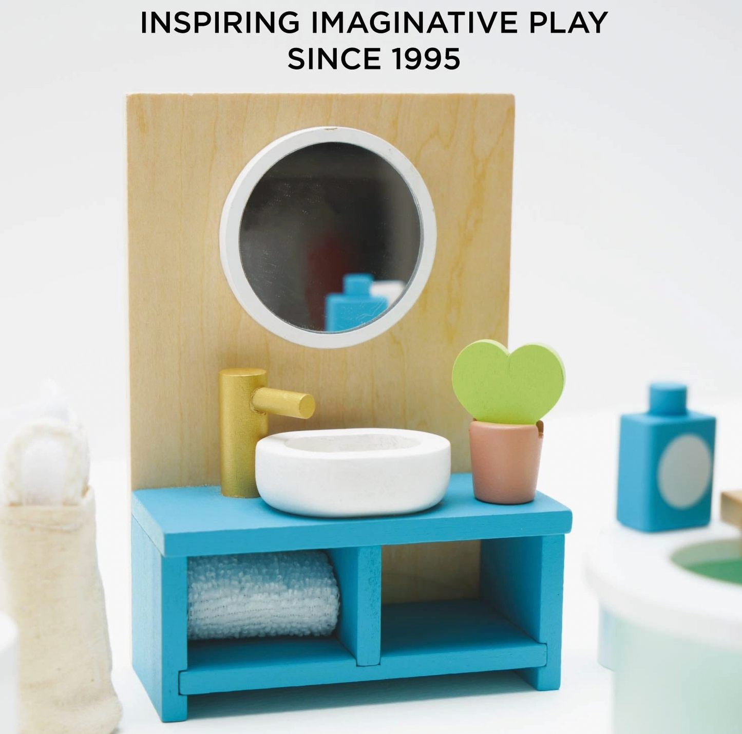 Le Toy Van wooden bathroom dolls house furniture set — close-up detail of the teal open vanity unit with round mirror panel, white vessel sink, gold tap, rolled blue towel on shelf and miniature heart-leaf cactus in a terracotta pot; "Inspiring Imaginative Play Since 1995" text