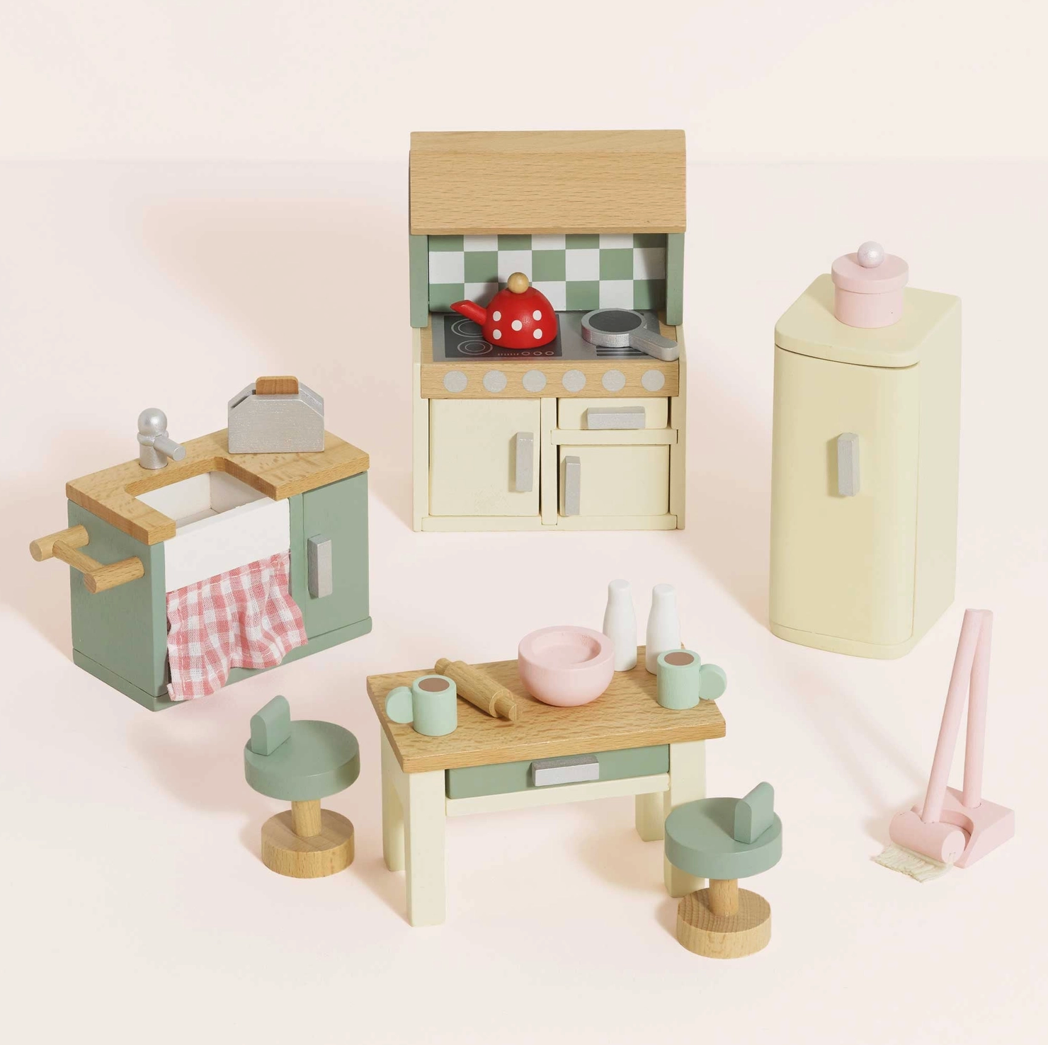 Le Toy Van 20-piece kitchen dolls house furniture set — styled scene showing cream cooker unit with sage green checkerboard splashback and red polka-dot kettle, sage green sink unit with pink gingham curtain, cream retro fridge-freezer, wooden kitchen island with two sage green bar stools, and pink mop and dustpan set