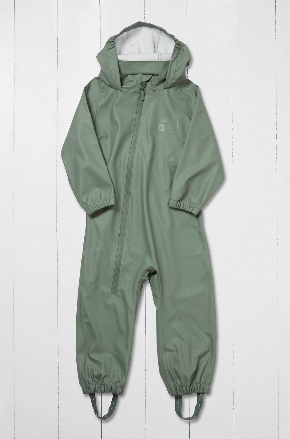 Grass & Air children's waterproof puddle suit in muted sage khaki green — front view flat lay on white background showing attached hood, waterproof front zip with zip guard, long sleeves with elasticated cuffs, full-length legs with elasticated ankles and integrated boot stirrups in matching khaki webbing