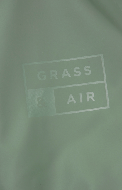 Grass & Air children's waterproof puddle suit in muted sage khaki green — lifestyle image of a child wearing the puddle suit outdoors