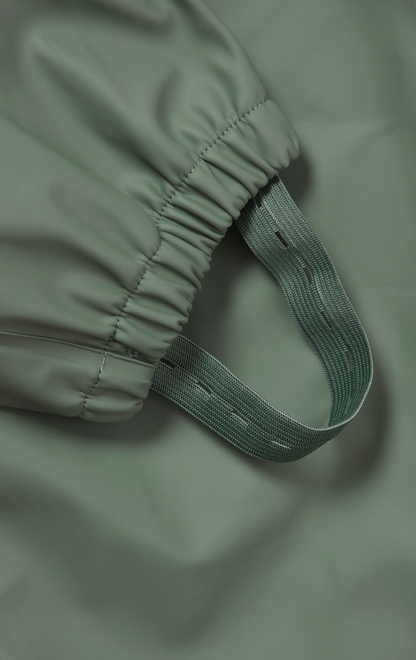 Grass & Air children's waterproof puddle suit — close-up detail of the elasticated ankle cuff and integrated boot stirrup in matching khaki webbing, designed to keep the suit neatly down over wellies