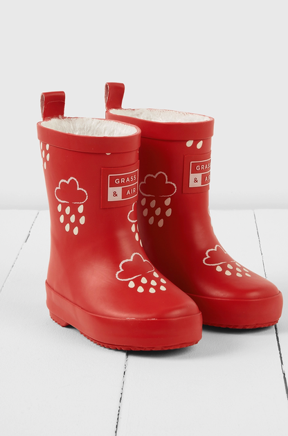 Grass & Air children's ruby red colour-changing wellies — dry state showing rich ruby red natural rubber with cream cloud-and-raindrop motifs, soft cream fleece lining visible at top, two pull-on loops at back and Grass & Air logo badge on side