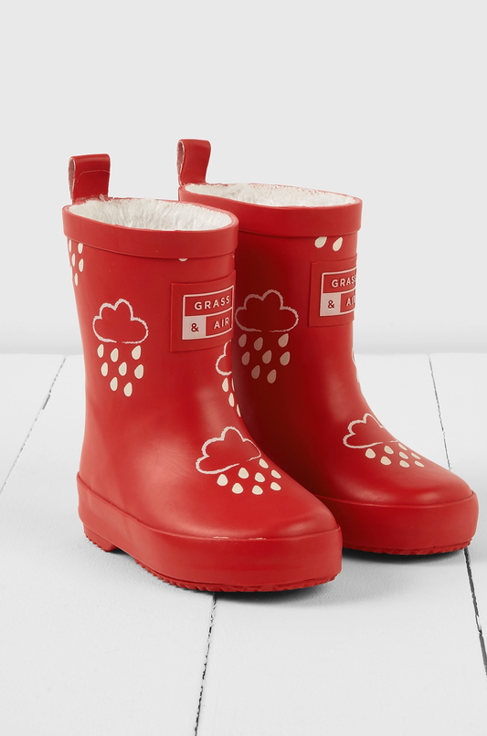 Grass & Air children's ruby red colour-changing wellies — dry state showing rich ruby red natural rubber with cream cloud-and-raindrop motifs, soft cream fleece lining visible at top, two pull-on loops at back and Grass & Air logo badge on side