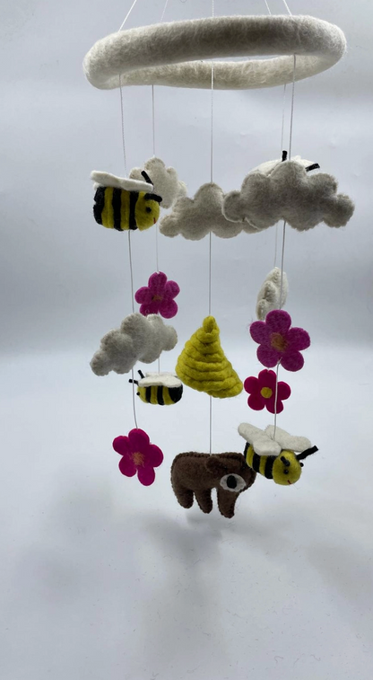 Funky Yak handmade needle-felted bears and bees nursery cot mobile — close-up three-quarter view showing the white felt ring hoop and the detail of the three bees with yellow-and-black stripes and white wings, the brown bear with white wings, the golden beehive, grey-white clouds and hot pink daisy flowers with yellow centres