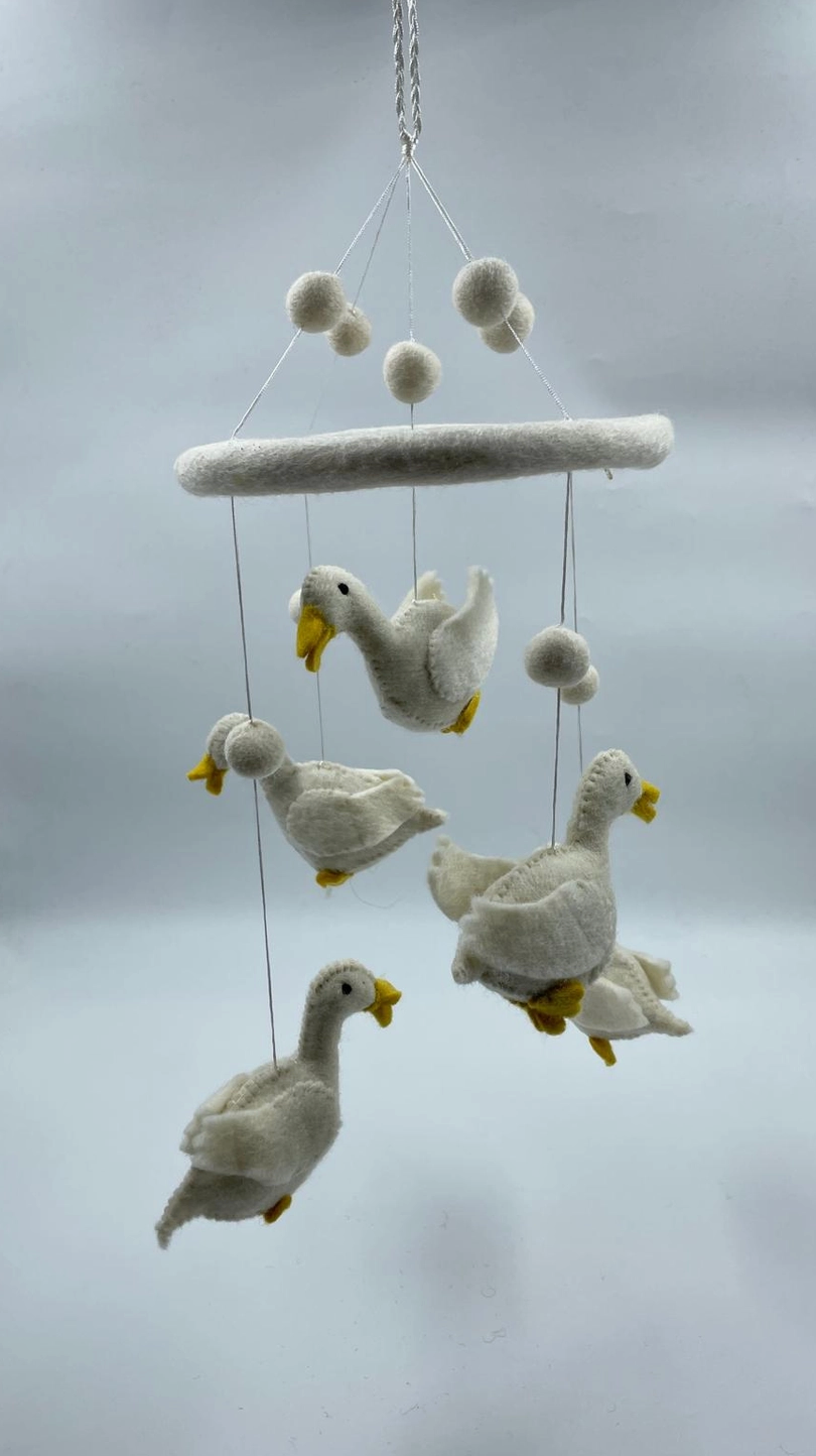 Funky Yak handmade needle-felted goose nursery cot mobile — full view showing five white felt geese with yellow beaks and feet suspended at staggered heights on fine silver wire from a white felt hoop, interspersed with white felt pom-pom balls; approximately 50cm from hoop to lowest point