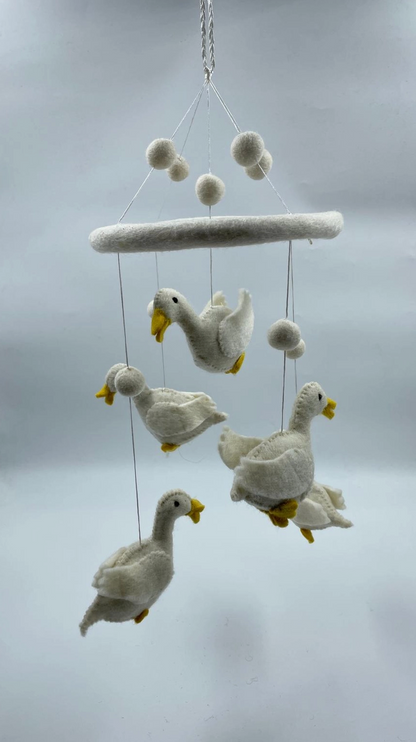 Funky Yak handmade needle-felted goose nursery cot mobile — full view showing five white felt geese with yellow beaks and feet suspended at staggered heights on fine silver wire from a white felt hoop, interspersed with white felt pom-pom balls; approximately 50cm from hoop to lowest point