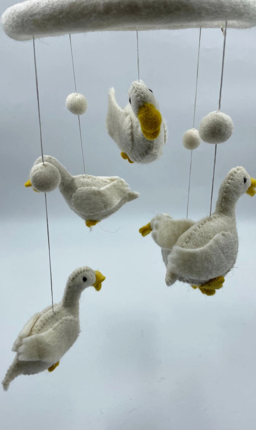 Funky Yak handmade needle-felted goose nursery cot mobile — close-up detail showing three of the five white felt geese with yellow beaks and feet and white felt pom-pom ball accents, suspended on fine silver wire from the white felt hoop