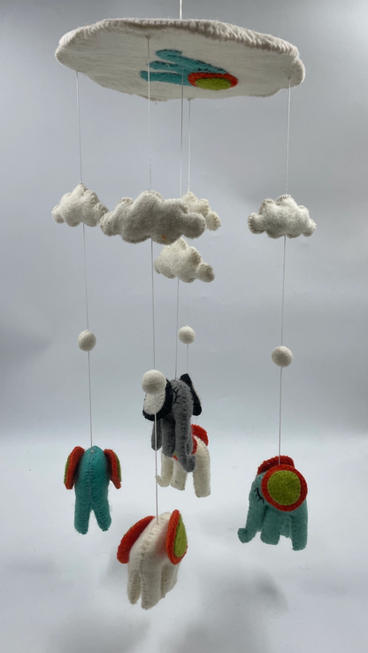 Funky Yak handmade needle-felted elephant nursery cot mobile — full front view showing five teal and charcoal grey elephants with bold red, orange and lime green circular ear decorations, suspended at staggered heights on fine silver wire from a large white felt cloud-shaped hoop with teal elephant and yellow-orange sun appliqué; three white felt cloud shapes and white pom-pom ball spacers mid-wire
