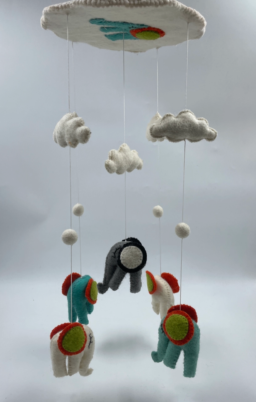 Funky Yak handmade needle-felted elephant nursery cot mobile — three-quarter view showing the cloud-shaped white felt hoop with teal elephant and sun appliqué, three white felt clouds, white pom-pom spacers and five teal and grey elephants with colourful circular ear decorations