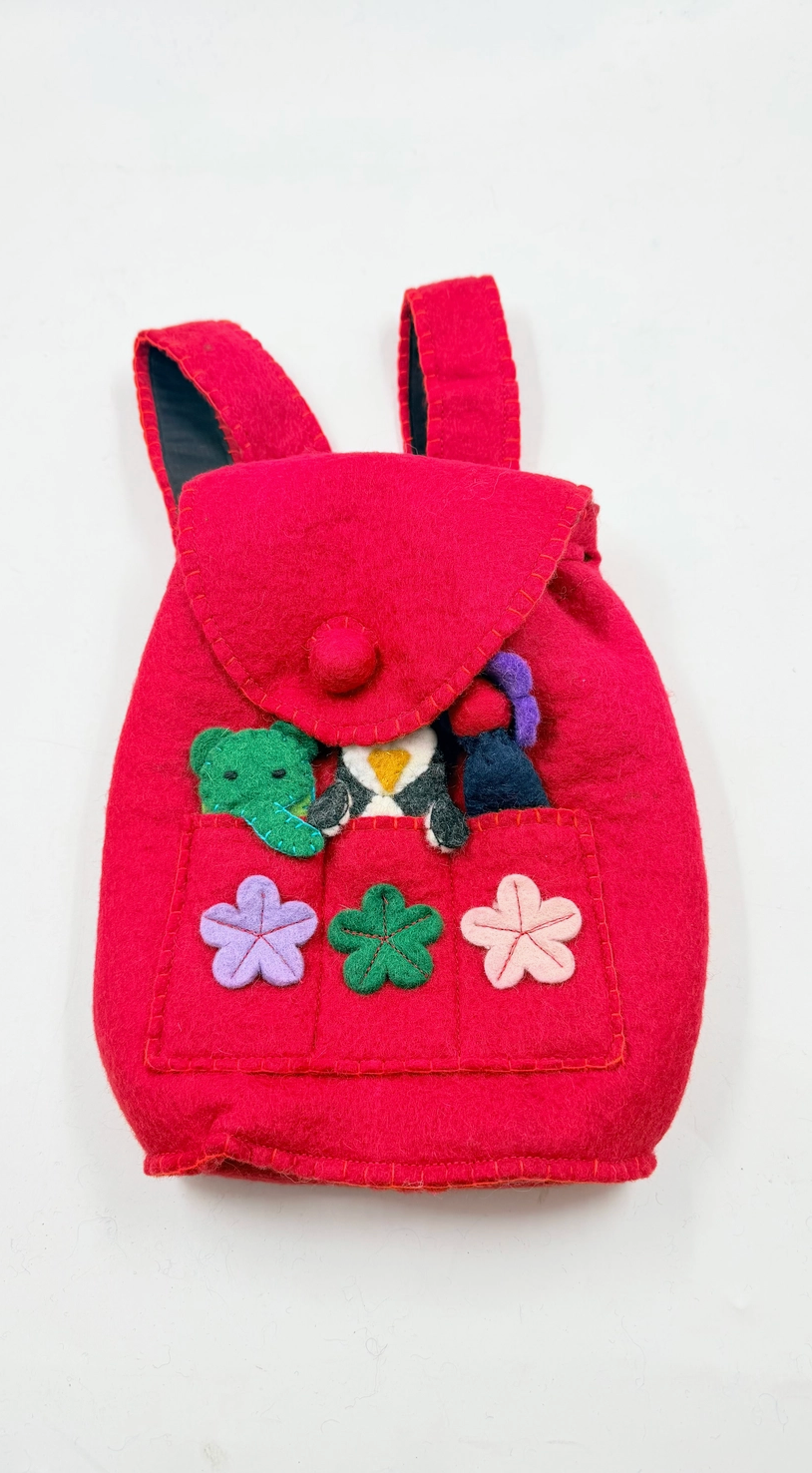 Funky Yak handmade red wool felt finger puppet backpack — front view flat lay showing pom-pom button flap, front pocket with appliquéd felt flowers in lavender, green and pink, and finger puppets including a green crocodile and penguin peeking out