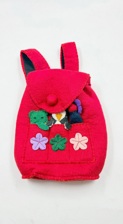 Funky Yak handmade red wool felt finger puppet backpack — front view flat lay showing pom-pom button flap, front pocket with appliquéd felt flowers in lavender, green and pink, and finger puppets including a green crocodile and penguin peeking out