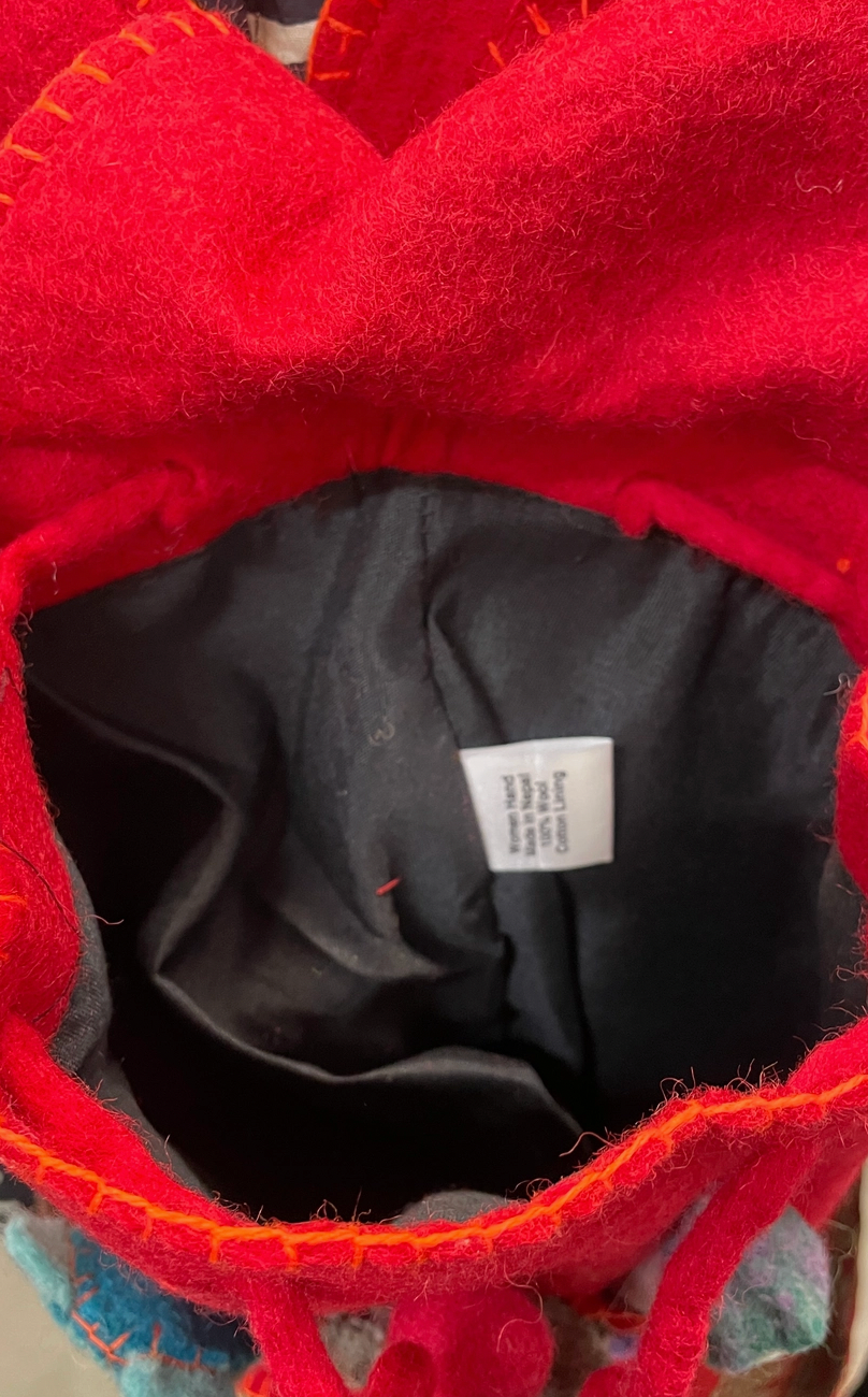 Funky Yak handmade red wool felt finger puppet backpack — lifestyle close-up detail of the front pocket showing the five felt finger puppets and appliquéd flower decorations