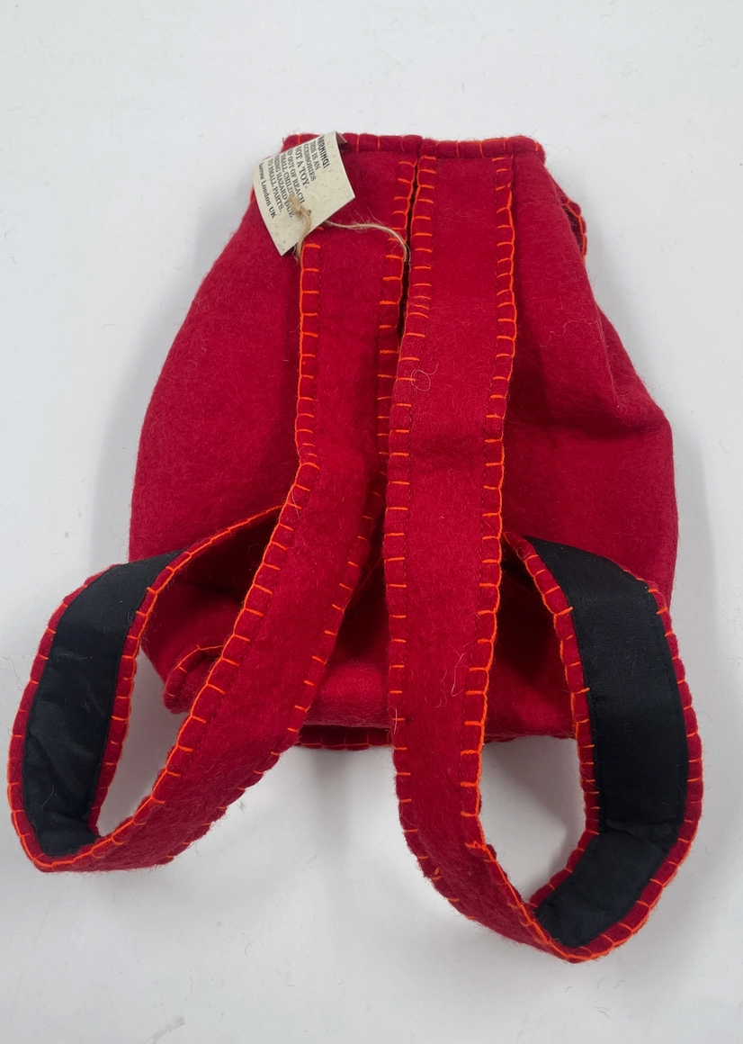 Funky Yak handmade red wool felt finger puppet backpack — back view with swing tag showing the padded navy-lined straps and orange blanket-stitch construction detail