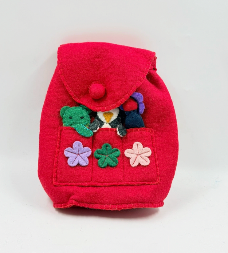 Funky Yak handmade red wool felt finger puppet backpack — front view showing pom-pom button flap closure, front pocket with three appliquéd felt flowers in lavender, green and pink, and finger puppets including a green crocodile and penguin peeking out of the pocket