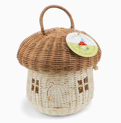 Rex London Wonders of Nature rattan mushroom house decorative basket — front view with circular card swing tag reading "Wonders of Nature Rattan Mushroom House" with illustrated red toadstool; showing honey-brown domed cap, pale cream body with arched doorway and wooden bead closure