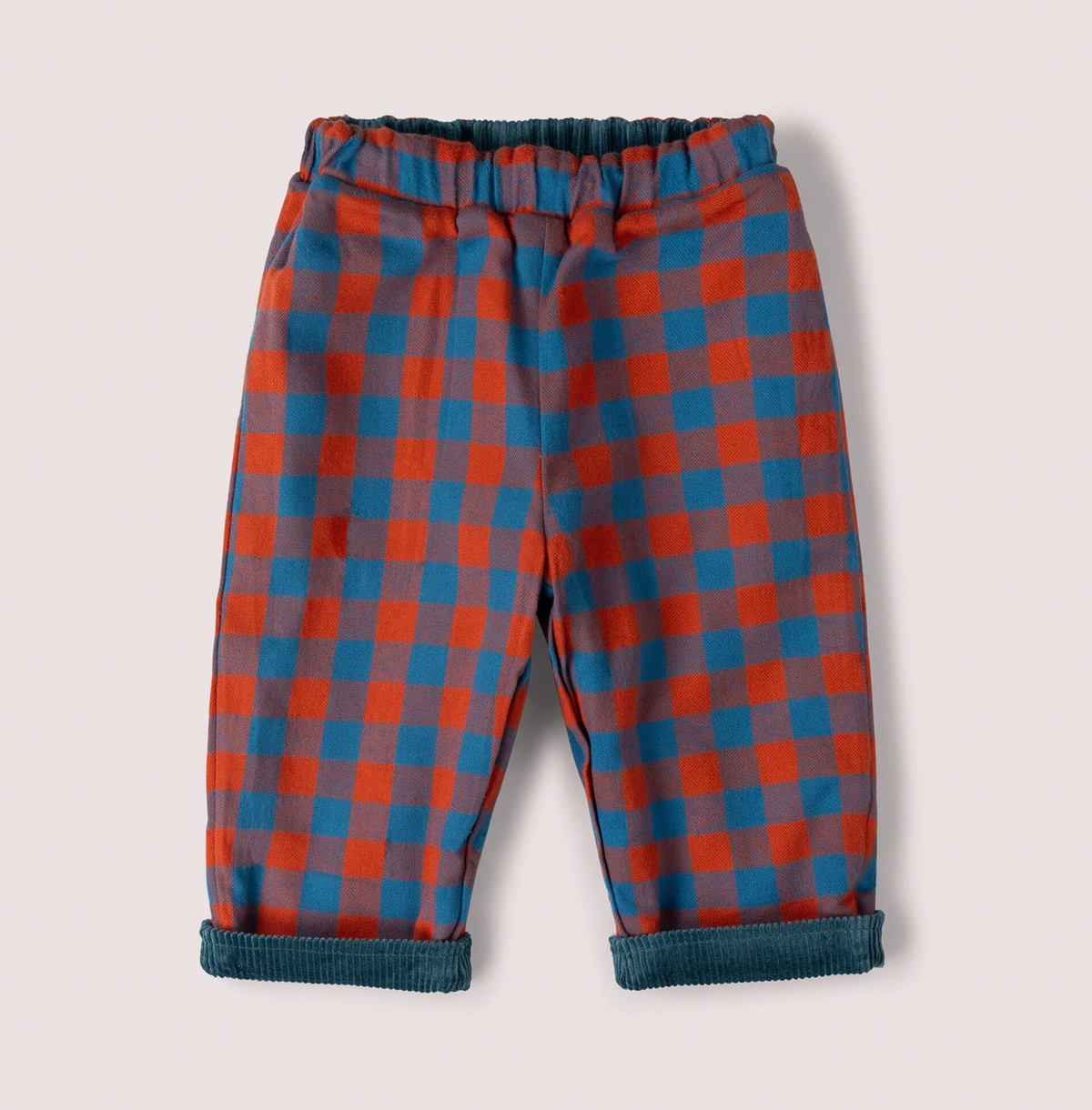 Little Green Rascals Calm Sea Check reversible pull-on trousers — check side showing bold burnt ochre and teal blue check brushed cotton with teal corduroy peeking at the elasticated waistband and turn-up cuffs; roomy relaxed fit