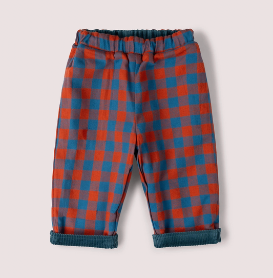 Little Green Rascals Calm Sea Check reversible pull-on trousers — check side showing bold burnt ochre and teal blue check brushed cotton with teal corduroy peeking at the elasticated waistband and turn-up cuffs; roomy relaxed fit