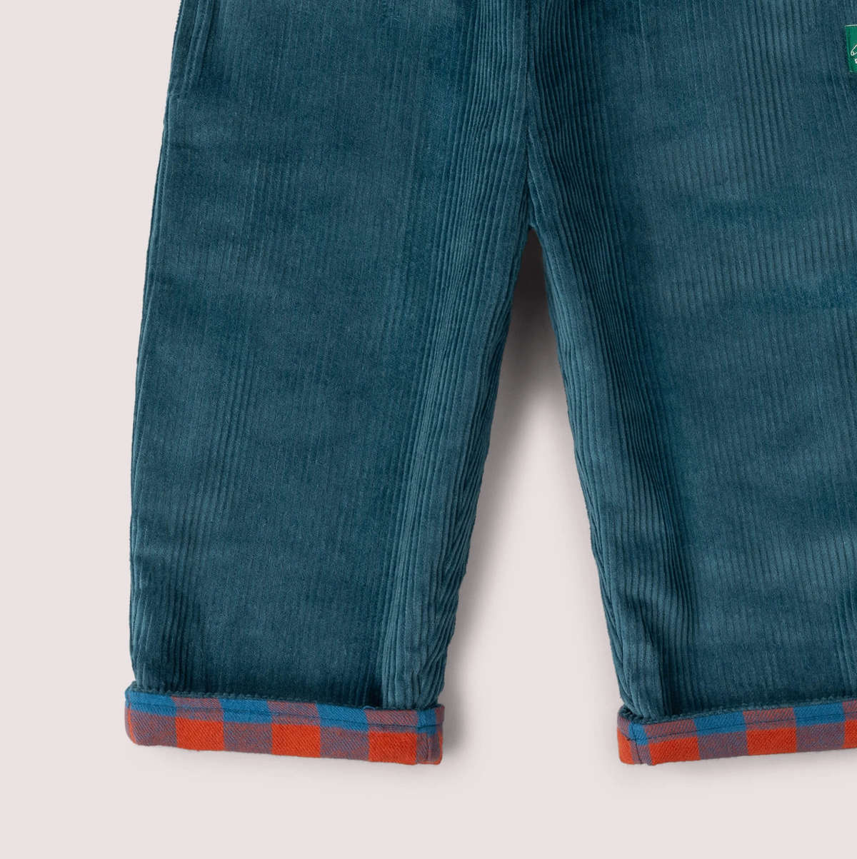 Little Green Rascals Calm Sea Check reversible pull-on trousers — close-up of the corduroy side turn-up cuffs showing the rich teal wide-wale corduroy legs with the burnt ochre and teal blue check brushed cotton lining turned up and visible at the hem