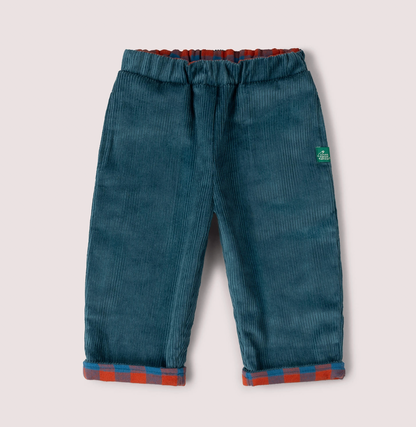 Little Green Rascals Calm Sea Check reversible pull-on trousers — corduroy side showing rich teal wide-wale corduroy with burnt ochre and teal blue check fabric peeking at the elasticated waistband and turn-up cuffs; Little Green Rascals green woven label badge on the right hip; roomy relaxed fit