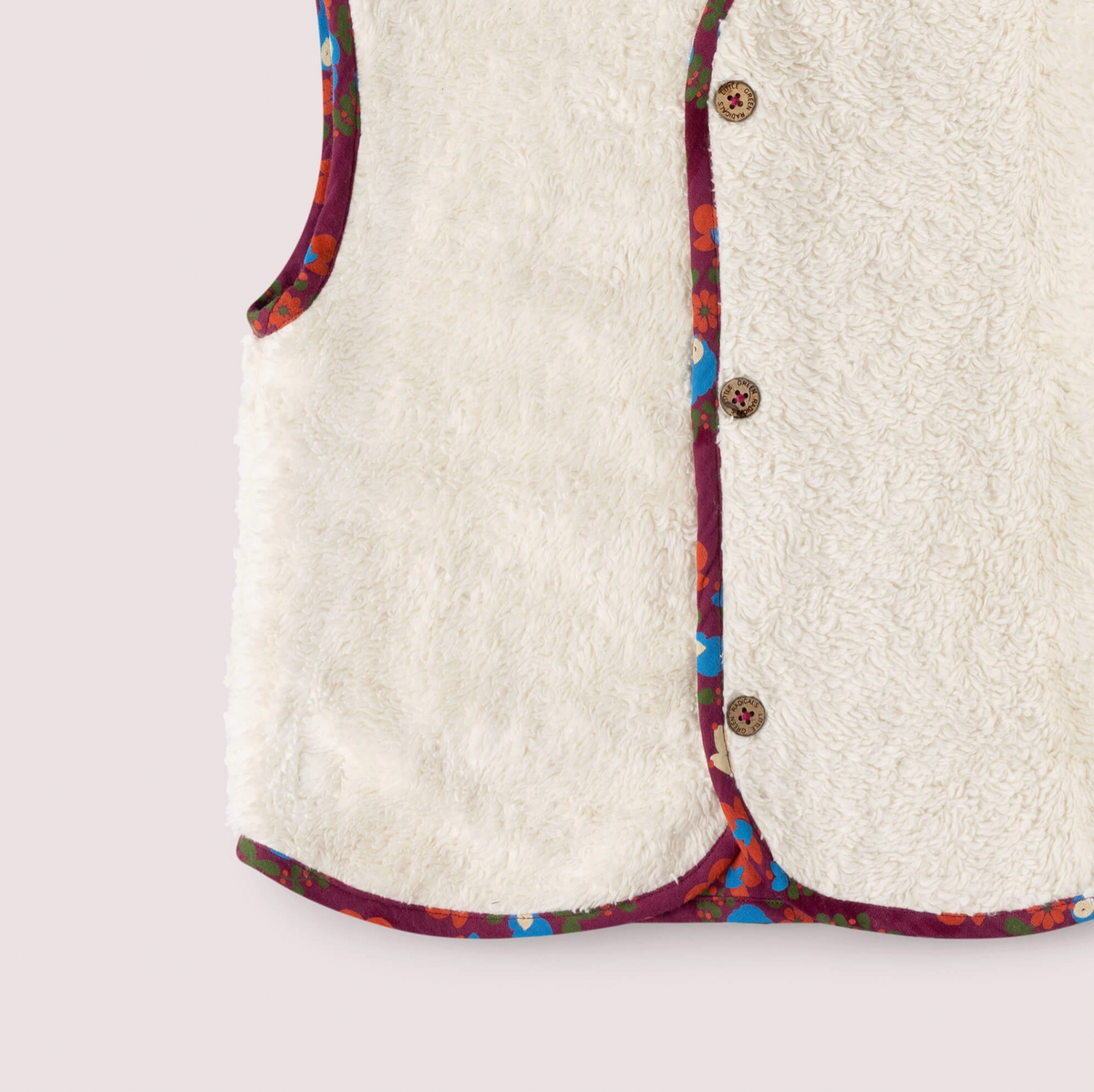 Little Green Rascals Folk Birds reversible gilet — close-up of the lower sherpa side showing the thick fluffy natural cream organic sherpa fabric with the folk birds print contrast binding trim at the hem and button placket, and branded coconut shell buttons